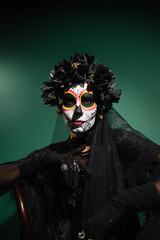 Woman in creepy day of death costume looking at camera on green background.