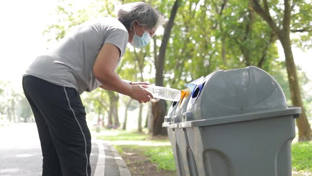 Asian elderly woman Take plastic bottles and throw them in the trash. Concept of keeping clean, separating plastic waste to reduce global warming. Recycle Plus