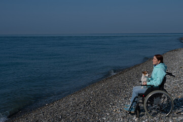 A serene Caucasian woman in a wheelchair is resting on the seashore with a jack russell terrier dog.