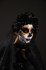 woman in dark halloween costume and sugar skull makeup looking away isolated on black.
