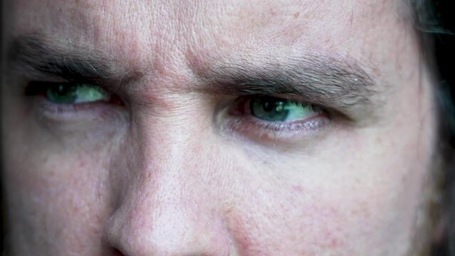 Man's gaze looking around. Extreme close up of green eyes of worried man who looks left and right. Tension, attention and fear. Intense gaze and frowning brow.