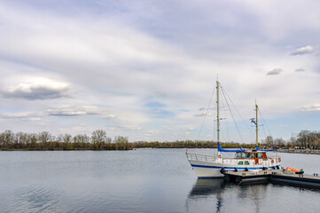 Fototapeta premium A wooden sailboat moored at a pontoon in the Obolon district, on the Dnieper River in Kiev, Ukraine, under a beautiful blue and cloudy sky, during the hot summer days.