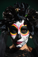 Portrait of woman with catrina makeup and black flowers on wreath isolated on dark green.