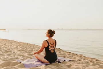 Fototapeta na wymiar Caucasian woman practicing yoga at seashore sandy beach on sunrise. Womens health and wellness. Sports body positive. Real instructor poses