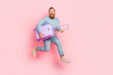 Full body portrait of astonished energetic man jump hurry rush hands hold suitcase isolated on pink color background