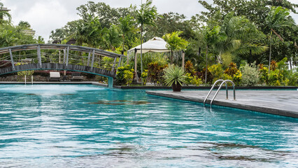 Swimming pool in the recreation area. An arched bridge over turquoise water, metal handrails of the...
