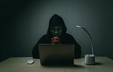 A hacker in black is using a laptop on a desk to hack the system.Cyber attack, system breaking and malware concept.