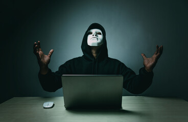 A hacker in black is using a laptop on a desk to hack the system.Cyber attack, system breaking and malware concept.