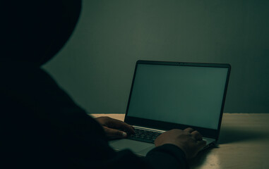 A hacker in black is using a laptop on a desk to hack the system.Cyber attack, system breaking and malware concept.