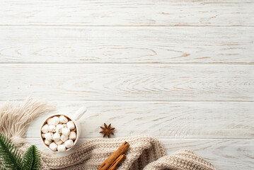Winter mood concept. Top view photo of mug of hot drinking with marshmallow spruce branch cozy knitted scarf anise and cinnamon sticks on white wooden desk background with copyspace