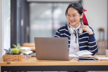 Fototapeta na wymiar Young adult happy smiling Hispanic Asian student wearing headphones talking on online chat meeting using laptop in university campus or at virtual office. College female student learning remotely. 