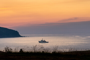 Superb landscape at sunset with a boat, isolated, close to the mainland, in a bay. Orange and purple coloured sky. Reflections of the sky on the water.