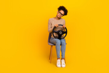 Full size photo of young lady sit armchair hold steering-wheel traffic isolated over yellow color...