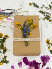 A gift box made of craft paper is decorated with dried pressed flowers and tied with a rope. DIY gift idea.