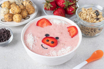 Fun food for kids - smoothie-bowl in shape funny piglet, with strawberries, granola, chocolate and crispy balls on gray background