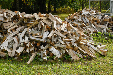 A large pile of firewood on the meadow. Trees has been cut and split into firewood to be used as fuel for heating in fireplaces and furnaces. Firewood pile. Shallow depth of field