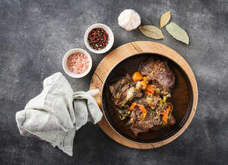 Traditional German braised beef cheeks in brown red wine sauce with herbs as closeup in skillet.
