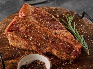 Raw fresh meat T-bone steak, seasoning on chopping cutting wooden board on grey background.