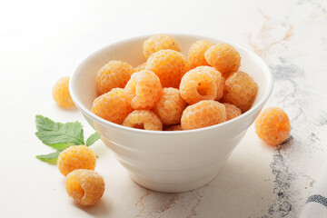 Ripe yellow raspberries in a bowl with a tea towel on a marble background. A bowl full of raspberries. Dessert ingredients.