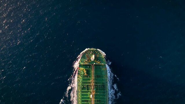 Aerial top down view of a general cargo bulk carrier ship traveling with speed over blue ocean with sunset light