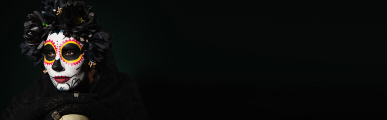 Woman in black wreath and sugar skull makeup looking away black on dark green background, banner.
