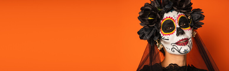 portrait of smiling woman in spooky halloween makeup and black wreath isolated on orange, banner.