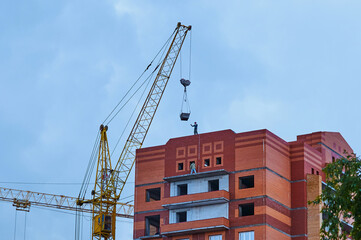 Construction site background. A high-rise red brick building is under construction. Crane near a...