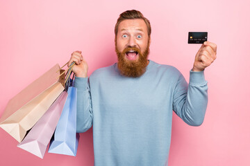 Photo of impressed excited man with red beard wear blue pullover hold shopping bags plastic card...
