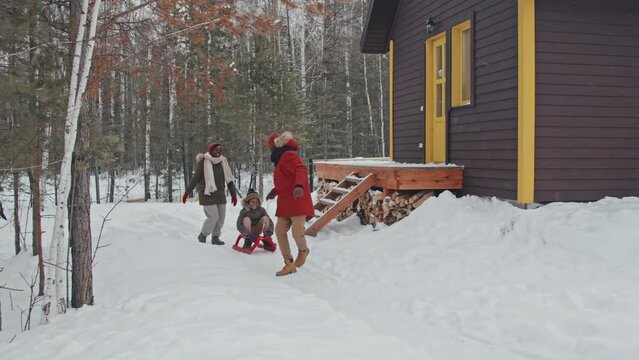 African American man, his wife and son enjoying winter day outdoors having fun running and sledging around their country house