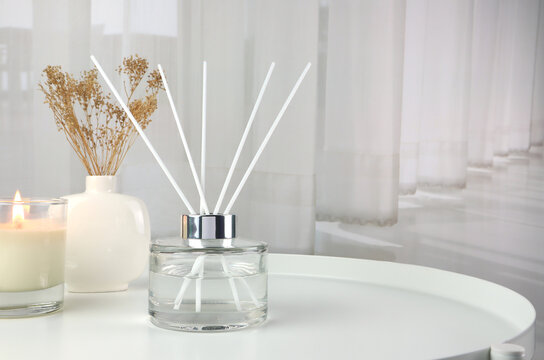 luxury aroma scent reed diffuser glass bottle is on white steel table with clear glass of scented candle and vase to creat romantic and relax ambient with background of nice white curtain in bedroom 