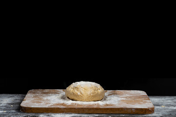 Making homemade dough for bread, pastry, and cookie. Wood board, spraying flour. Rural food cooking. Black background