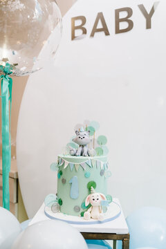 Birthday Cake for 1 year on background silver balloons. The cake with a figure wolf and rabbit decorated green and grey decor. Delicious reception at a birthday party. Photo wall and arch.