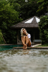 Swimming pool in a tropical villa. A young woman is sitting by the pool, enjoying the tranquility.