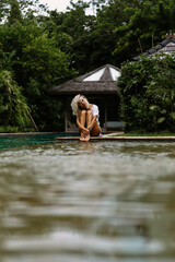 Swimming pool in a tropical villa. A young woman is sitting by the pool, enjoying the tranquility.