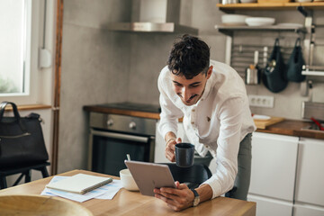 businessman drinking morning coffee at home and checking mails on tablet