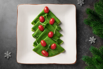 Christmas tree of vegan spinach crepes on ceramic plate. Healthy holiday food, vegan concept. dark...