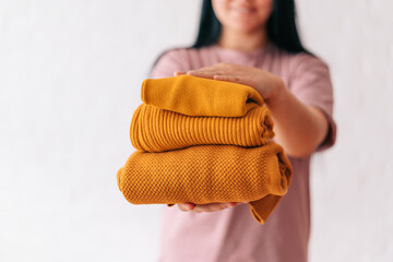 A slender young woman holding a large stack of folded knitted sweaters in her hands, a light chic style, various knitting patterns. Background, copy space. the concept of warmth and comfort