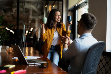 Colleagues laughing in office. Businesswoman and businessman drinking coffee.
