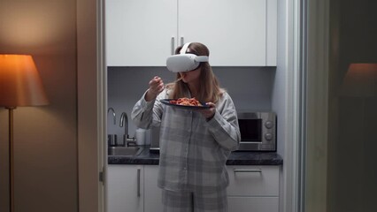 Metaverse futuristic world concept. Young woman in pajamas and vr goggles eat pasta standing in kitchen - Powered by Adobe