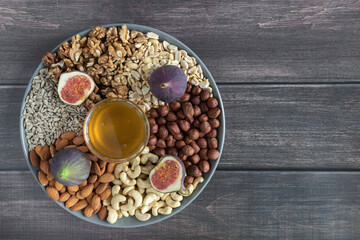 Flat plate with mixed nuts, honey, figs. Top view background with healthy snack on a wooden dark table