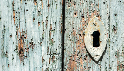 The old plank rotted with paint peeling off the keyhole. Wooden background. The texture of cracked paint in close-up.