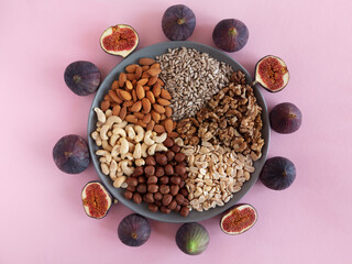 Flat plate with mixed nuts, seeds, figs. Top view background with healthy snack on pink background