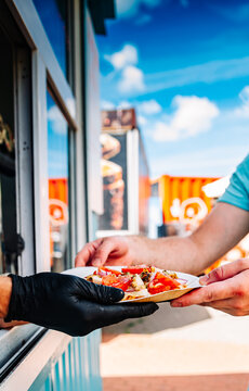 chef hands gives a pita mini pizza to man from food truck on street. street food, fast food.