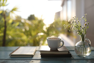 Tea cup and White Marguerite in glass vase and notebook on blue table outdoor