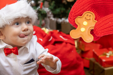 Little boy with a Santa Claus hat looks at gingerbread figurine in a hand