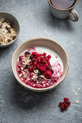 petit déjeuner bol de yaourt muesli, fruits secs, groseilles et framboises sur table