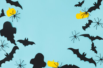Halloween flat lay. Black ghosts, spiders, bats and yellow pumpkins decorations on blue background flat lay. Happy Halloween! Card template with space for text. Modern minimal frame