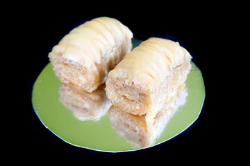 two slices of sweet honey baklava with crushed pistachios lie side by side on a mirror surface on a black background. Oriental sweets. macro. honey