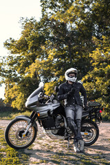 Fototapeta na wymiar rider guy use smart phone in jeans biker jacket and helmet sit on tourist touring motorcycle. outdoors, dual sport adventure concept, vertical photo, dirt road