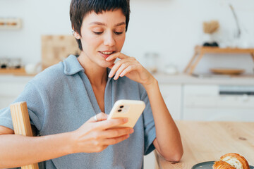 Young brunette woman sitting at home texting on mobile phone and browsing social media.